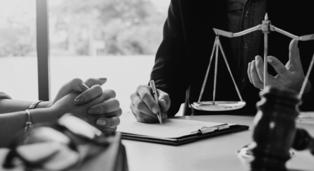 Male and female sitting at a desk with paper, a pen and the scales of justice