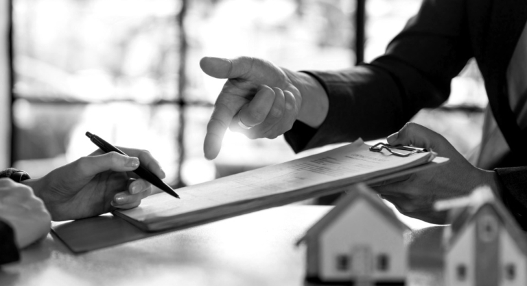 Photo of paperwork, the hands of two people and two small scale model houses