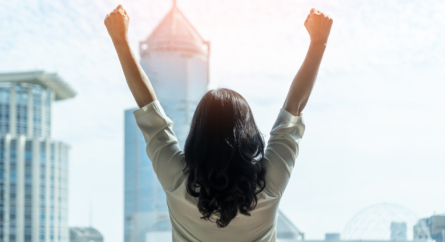 Woman facing the city with her back to camera and hands raised in the air