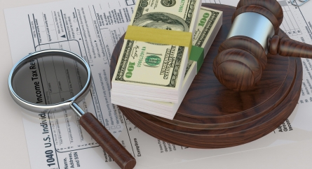 Magnifying glass, gavel, and stacks of money on an income tax return form